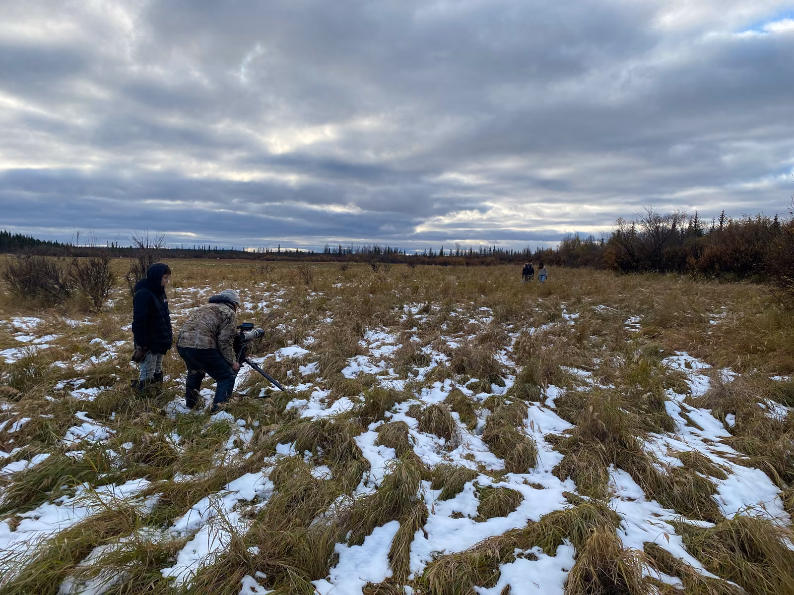 A small crew crossing snowy tundra under a wide Alaskan sky
