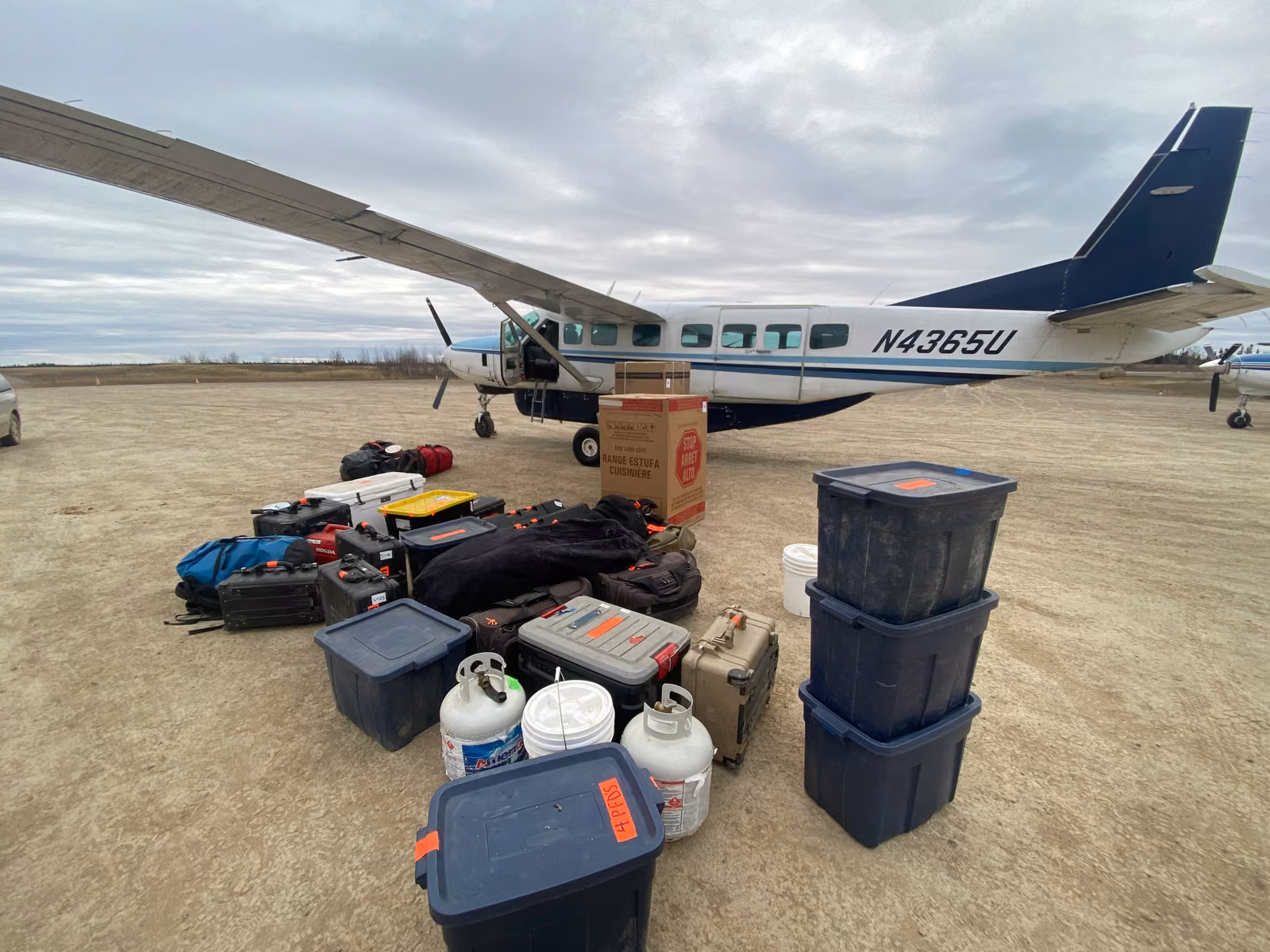 A bush plane on a gravel strip with gear unloaded beside it