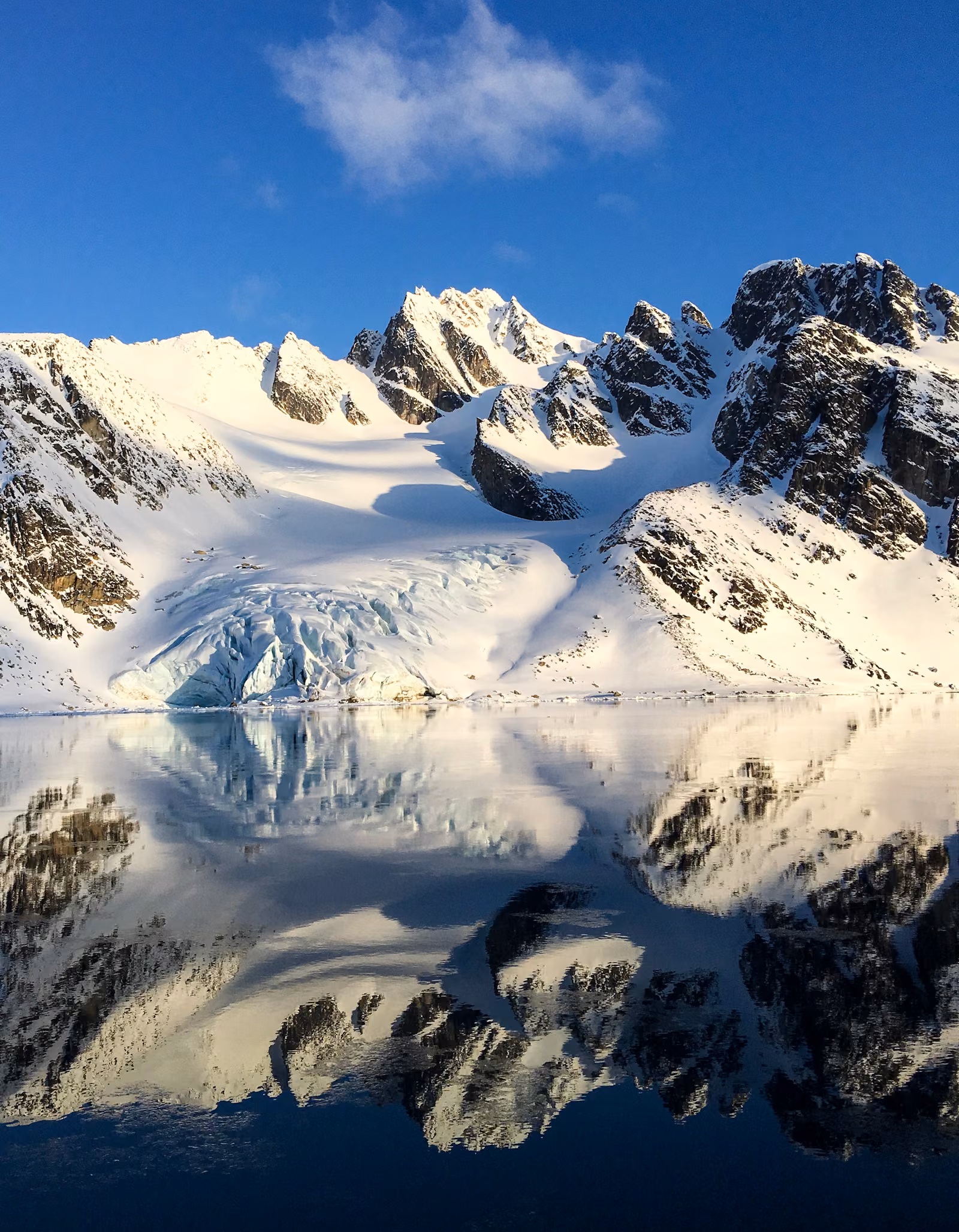 Jagged snow peaks mirrored in a glassy Svalbard fjord
