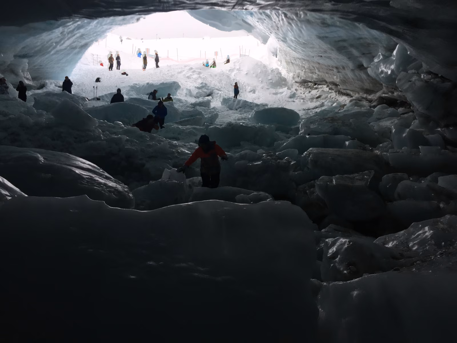 Tiny figures beneath the bright mouth of a glacier ice cave