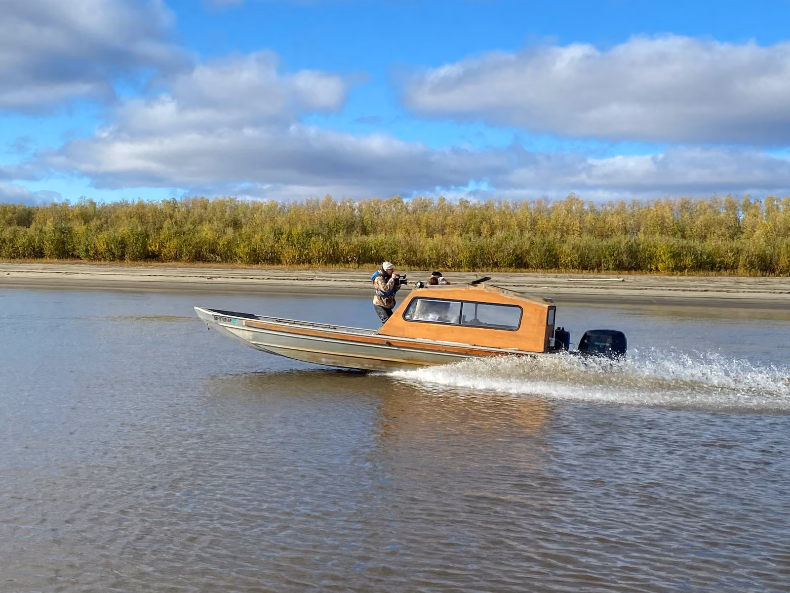 A skiff speeding along the Koyukuk River past the boreal forest