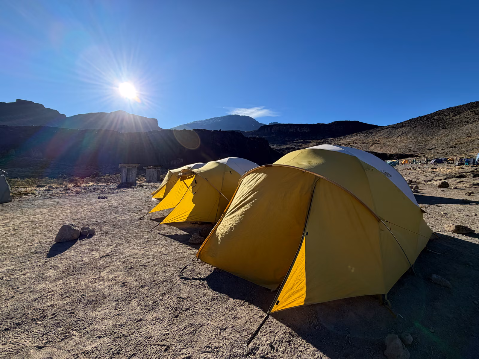 Yellow expedition tents on high volcanic scree under a bright sun