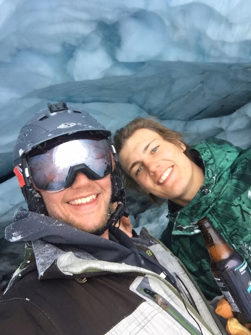 Two friends grinning in goggles inside a glacier ice cave