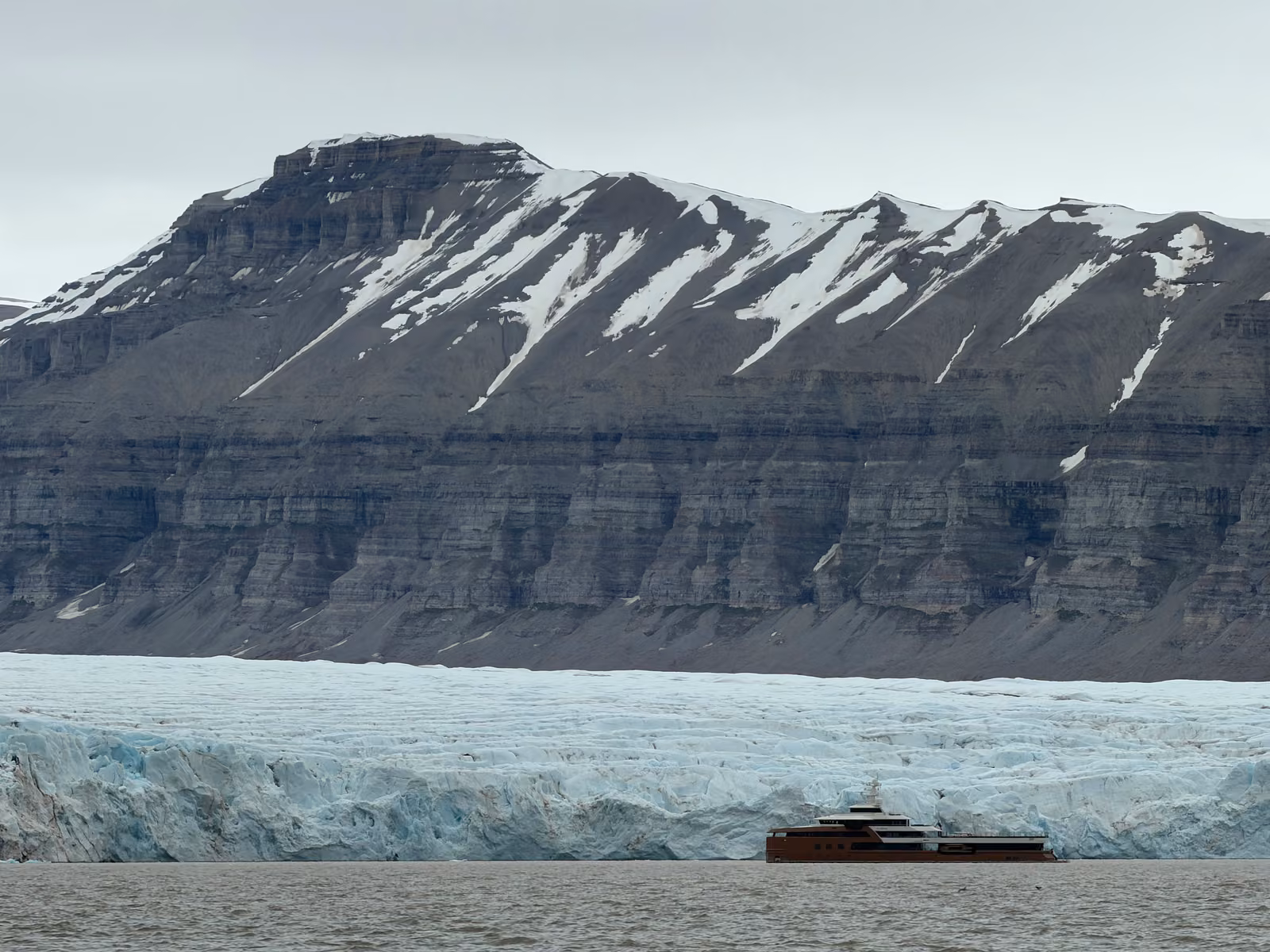 Snow streaked cliffs above a glacier front in a Svalbard fjord