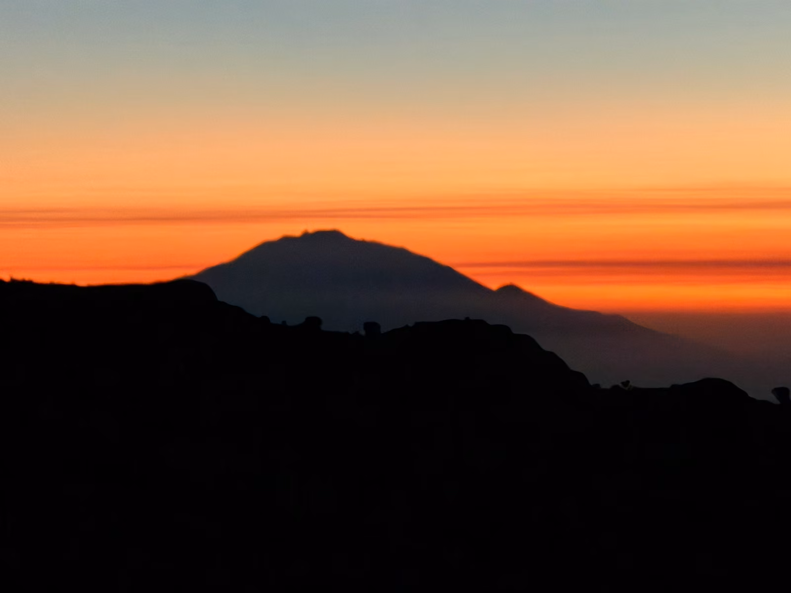 Mount Meru silhouetted against an orange dusk sky