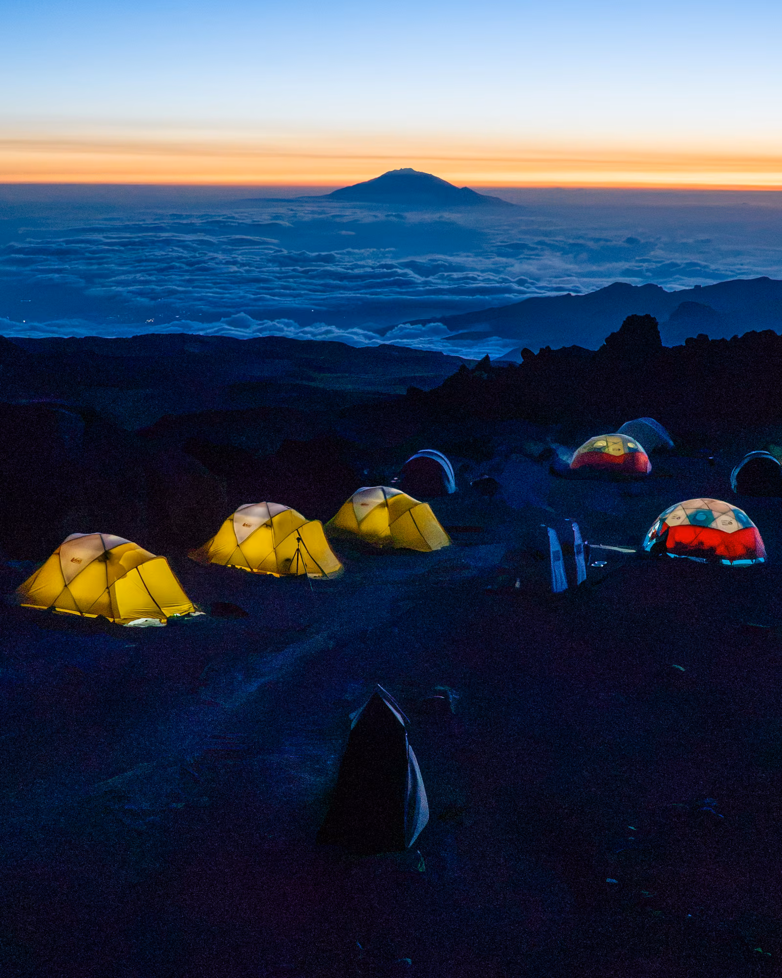 Lit tents at blue hour, Mount Meru floating above the clouds