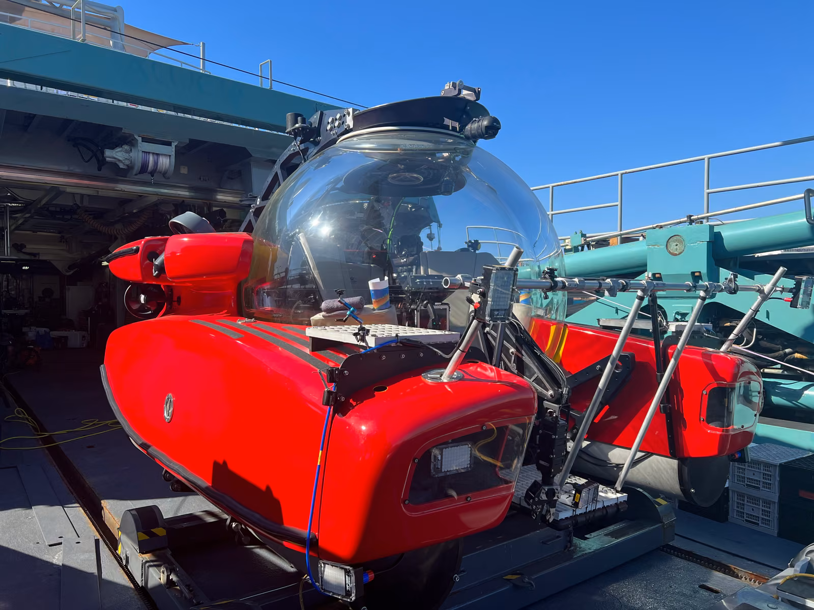 A red research submersible on deck under a clear Aegean sky