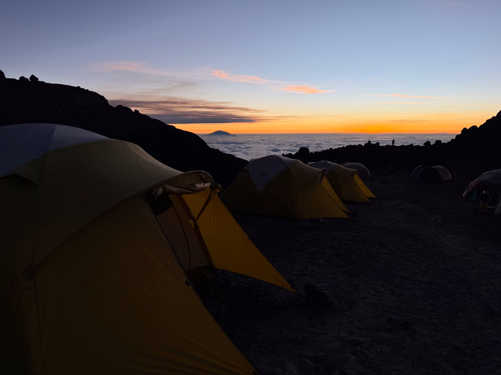 Yellow tents at a high camp above a sea of cloud at dusk
